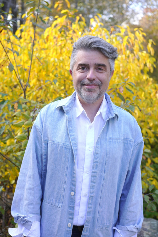 Roddy Schrock, smiling, in a pale denim shirt in front of yellow autumn leaves.